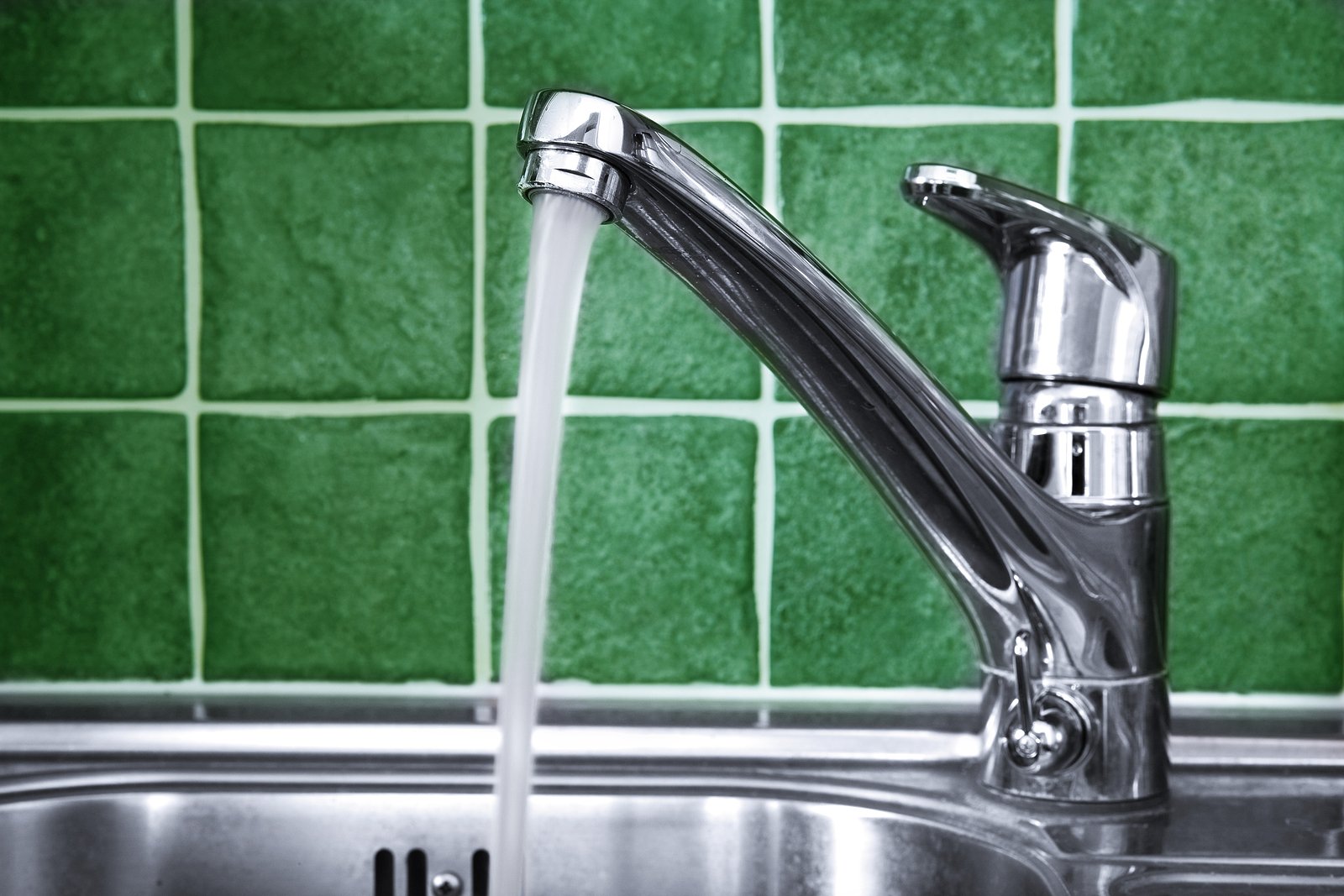 Water running from kitchen faucet with green tiles in background